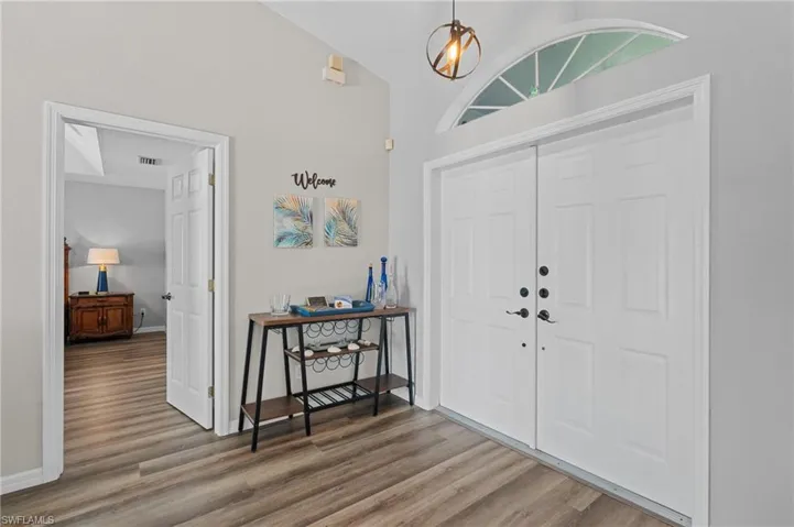 Foyer entrance featuring baseboards, visible vents, wood finished floors, and vaulted ceiling