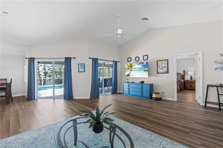 Living area featuring lofted ceiling, baseboards, visible vents, ceiling fan, and wood finished floors