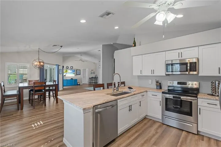 Kitchen featuring a sink, a peninsula, stainless steel appliances, ceiling fan with notable chandelier, and visible vents