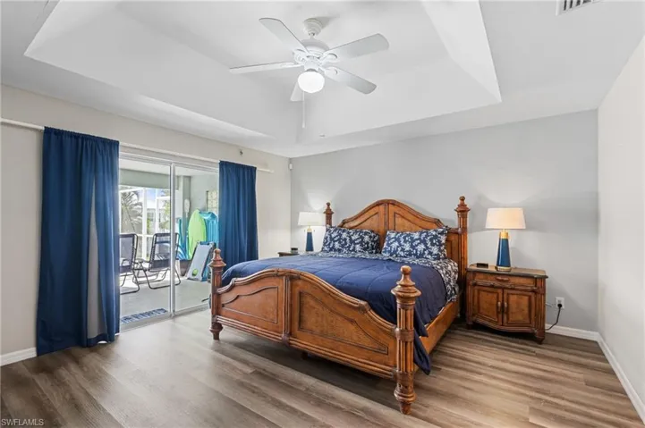 Bedroom featuring a tray ceiling, baseboards, wood finished floors, and access to outside