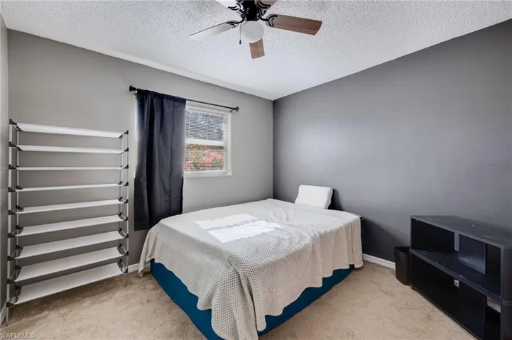 Bedroom featuring ceiling fan, light carpet, and a textured ceiling