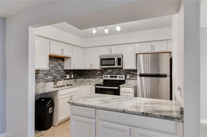 Kitchen featuring stainless steel appliances, light stone counters, white cabinets, decorative backsplash, and a peninsula