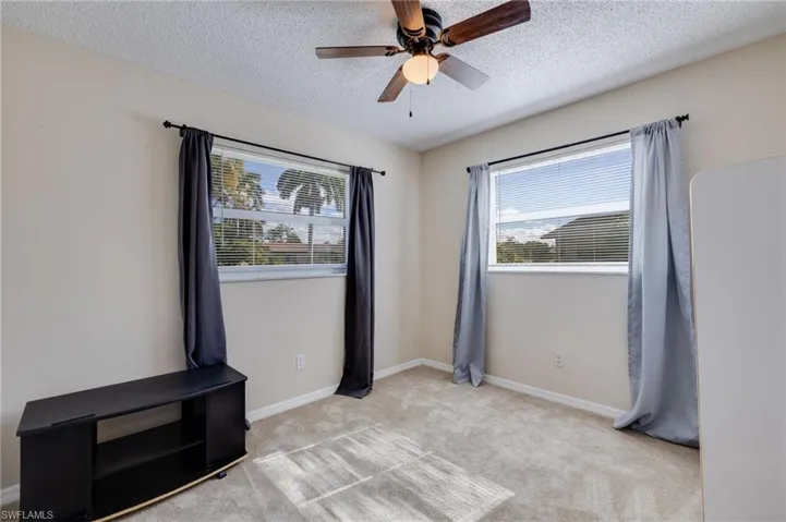 Unfurnished bedroom with ceiling fan, light colored carpet, a textured ceiling, and multiple windows