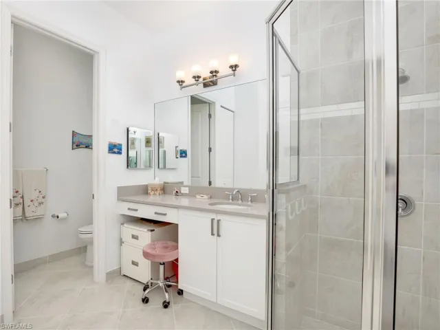 Bathroom featuring a shower with door, tile flooring, toilet, and vanity with extensive cabinet space