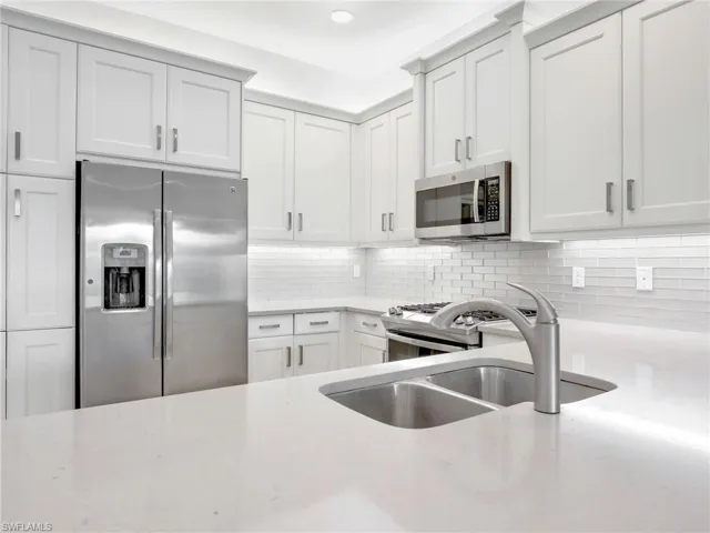Kitchen with tasteful backsplash, light stone counters, sink, white cabinetry, and appliances with stainless steel finishes