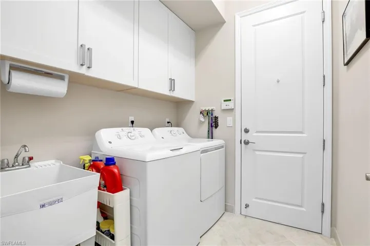 Washroom featuring washer and dryer, sink, light tile flooring, and cabinets