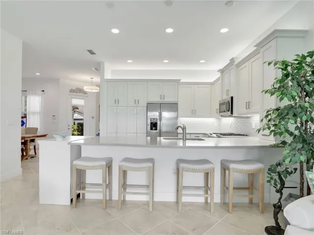 Kitchen featuring stainless steel appliances, backsplash, a breakfast bar, sink, and light tile flooring
