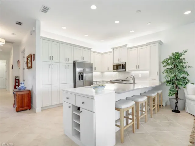 Kitchen with stainless steel appliances, light tile floors, white cabinetry, and backsplash