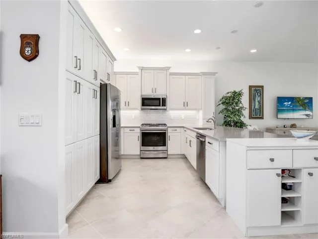 Kitchen with kitchen peninsula, tasteful backsplash, stainless steel appliances, light tile floors, and sink