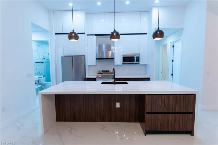Kitchen featuring appliances with stainless steel finishes, decorative light fixtures, white cabinetry, a kitchen island with sink, and dark brown cabinetry