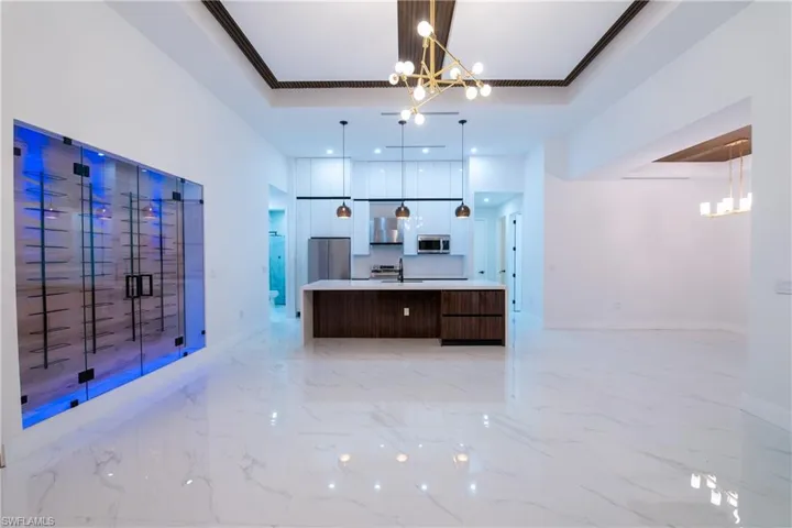 Kitchen with a large island with sink, a tray ceiling, a notable chandelier, and stainless steel appliances