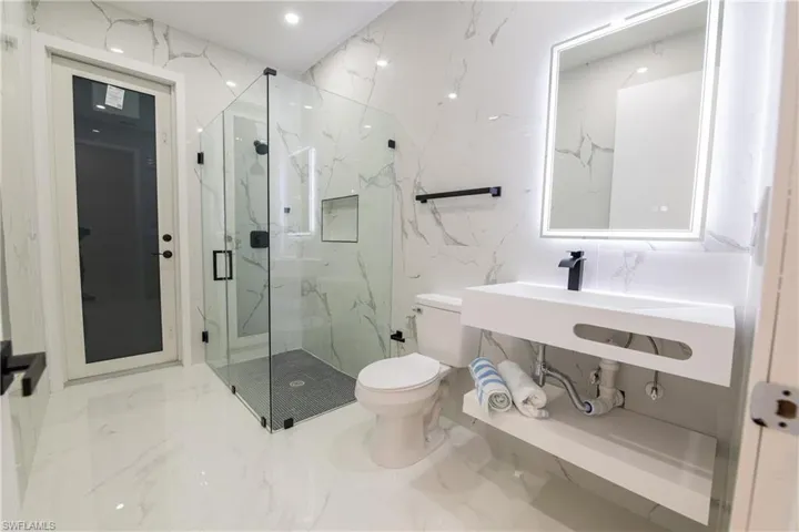 Bathroom featuring an enclosed shower, sink, and toilet