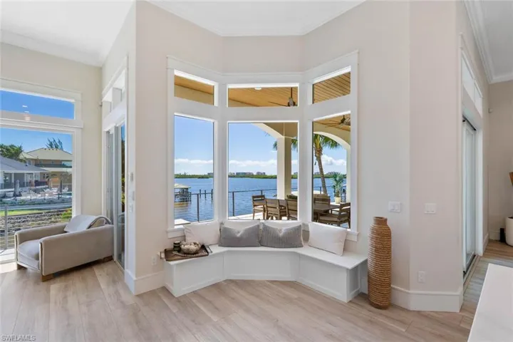 Living area with ornamental molding, light wood-style floors, a water view, a sunroom, and healthy amount of natural light