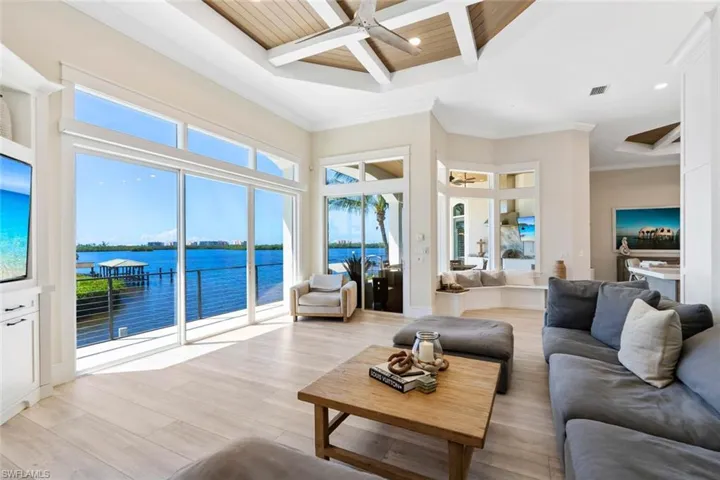 Living room featuring a water view, coffered ceiling, light wood-style floors, ceiling fan, and ornamental molding