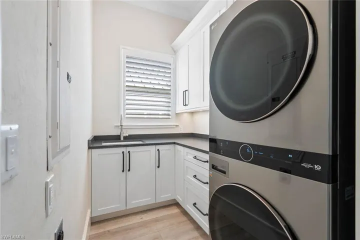 Washroom with stacked washer / dryer, light wood-style floors, cabinet space, and crown molding