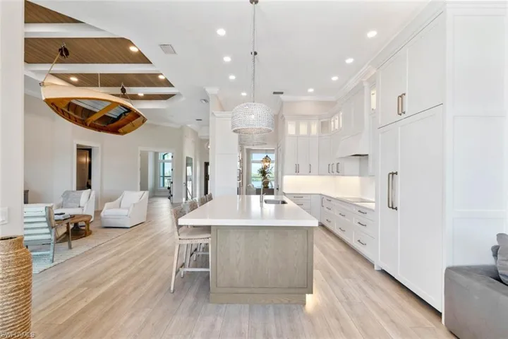 Kitchen with open floor plan, white cabinetry, a kitchen bar, glass insert cabinets, and recessed lighting