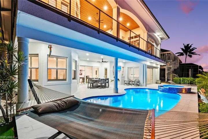 Pool at dusk with a balcony, outdoor dining space, a ceiling fan, a patio, and a pool with connected hot tub