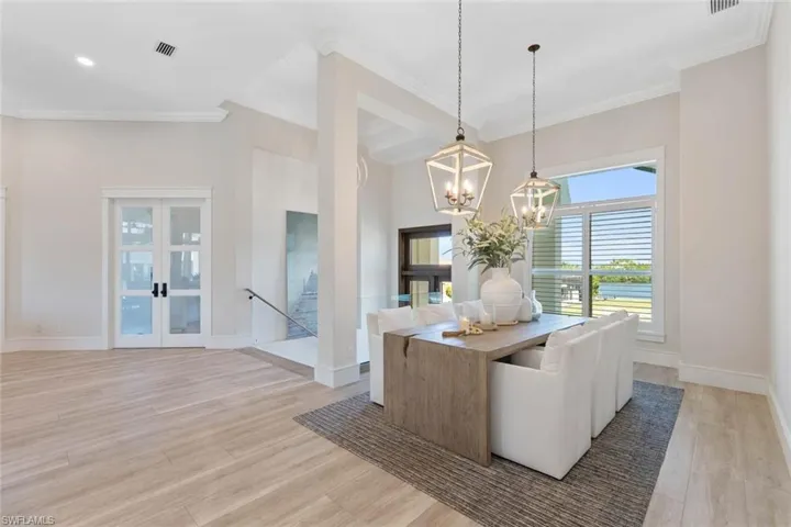 Dining room featuring french doors, crown molding, light wood-style floors, a towering ceiling, and a chandelier