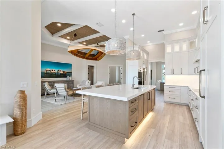 Kitchen featuring a kitchen island with sink, glass insert cabinets, pendant lighting, white cabinets, and beamed ceiling