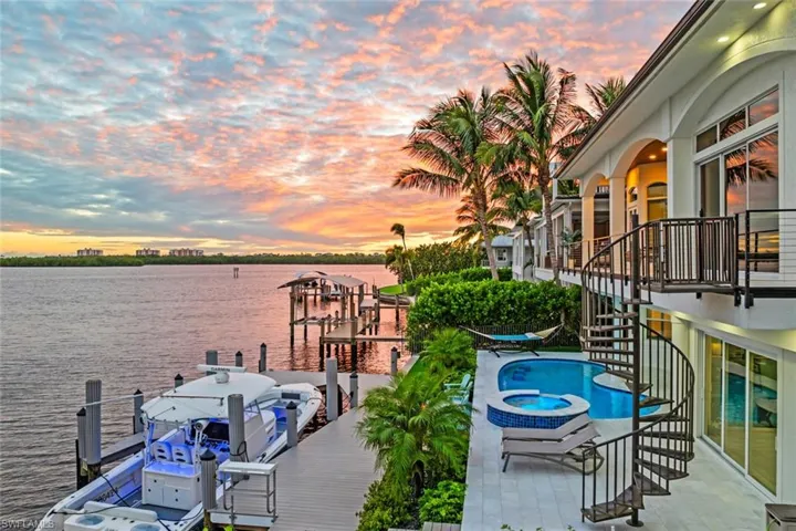Balcony at dusk with stairway, a water view, a dock, view of pool area, and a pool with connected hot tub