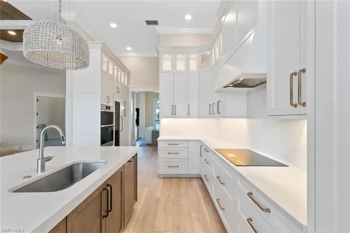 Kitchen with light wood finished floors, crown molding, white cabinets, glass insert cabinets, and light stone counters