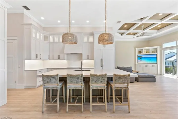 Kitchen featuring a kitchen breakfast bar, a kitchen island with sink, decorative light fixtures, a towering ceiling, and glass insert cabinets