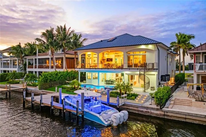Back of property featuring a water view, a patio area, stairway, an outdoor pool, and a balcony