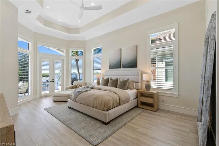Bedroom with a tray ceiling, access to exterior, ceiling fan, light wood-style floors, and a towering ceiling