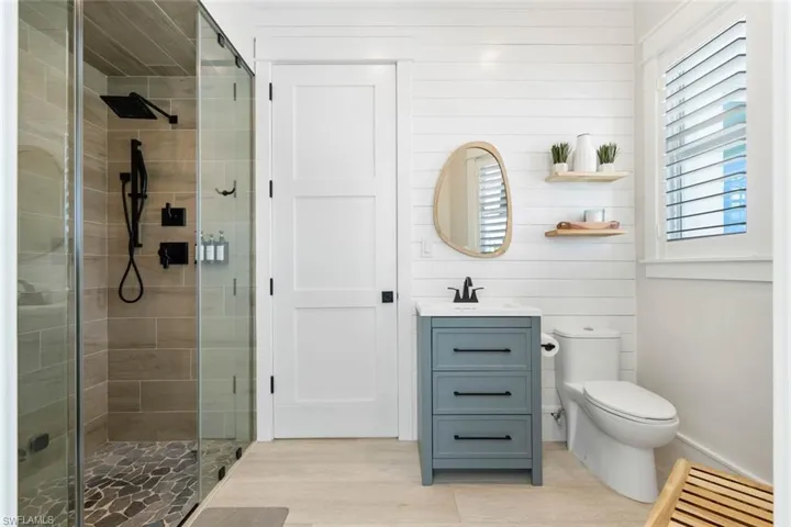 Bathroom with vanity, a shower stall, wooden walls, and light wood-style floors