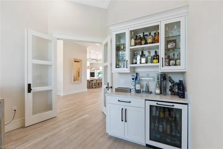 Indoor dry bar featuring open shelves, beverage cooler, white cabinets, glass insert cabinets, and light wood finished floors
