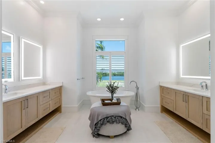 Bathroom with two vanities, a soaking tub, ornamental molding, recessed lighting, and a water view