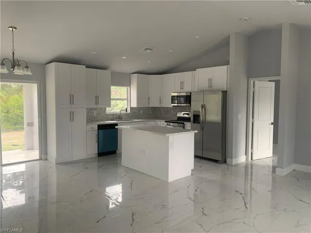 Kitchen with appliances with stainless steel finishes, a center island, light marble finish flooring, white cabinets, and recessed lighting