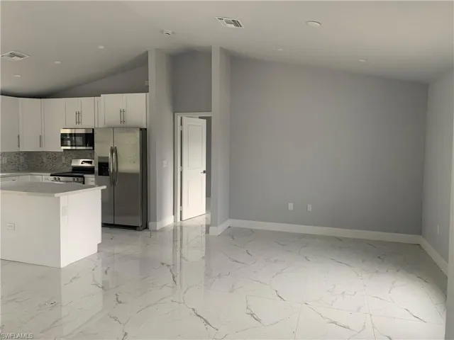 Kitchen featuring stainless steel appliances, white cabinets, light marble finish floors, vaulted ceiling, and tasteful backsplash