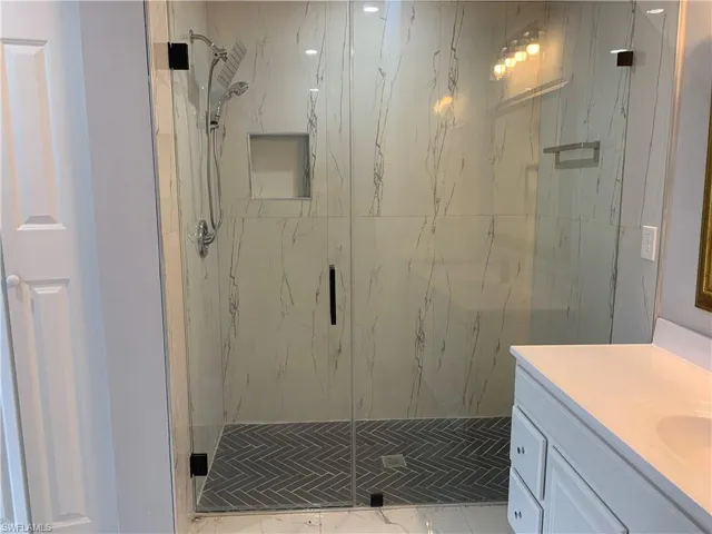 Full bath featuring a marble finish shower, vanity, and light marble finish floors