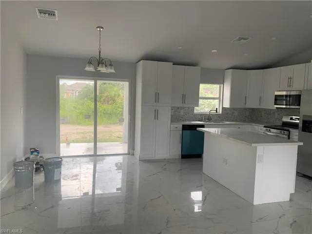 Kitchen featuring light marble finish floors, white cabinets, stainless steel appliances, hanging light fixtures, and tasteful backsplash