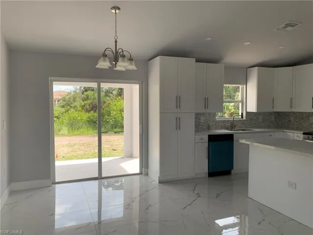 Kitchen featuring light marble finish floors, white cabinets, hanging light fixtures, dishwashing machine, and tasteful backsplash