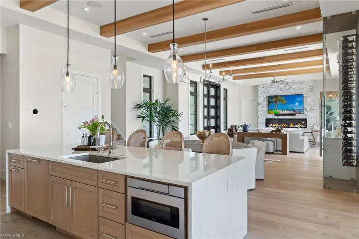 Kitchen featuring beamed ceiling, hanging light fixtures, light stone countertops, light wood-type flooring, and open floor plan