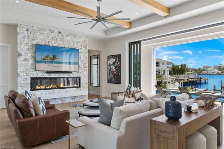 Living room featuring light wood finished floors, a fireplace, a ceiling fan, a water view, and a wooden ceiling with exposed beams