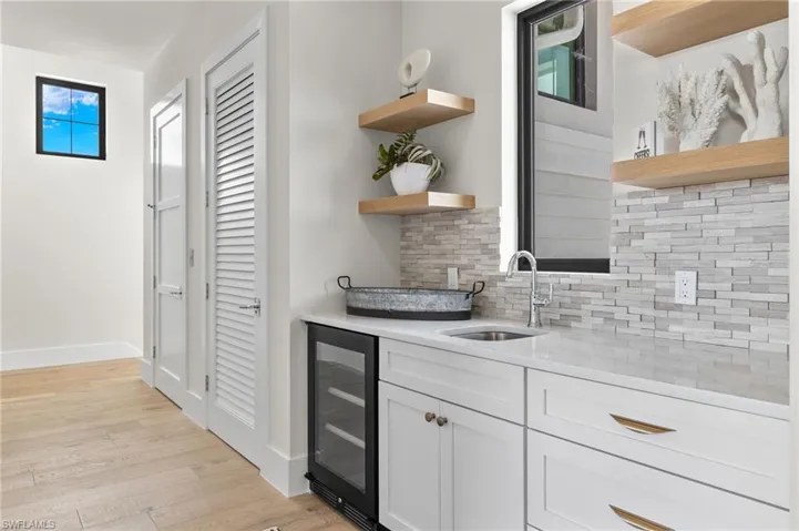 Bar area featuring open shelves, light stone counters, wine cooler, tasteful backsplash, and light wood-style flooring