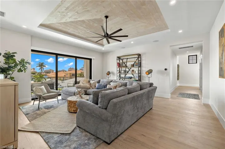Living room with light wood-type flooring, a raised ceiling, recessed lighting, and ceiling fan