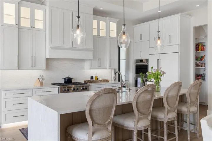 Kitchen with a breakfast bar area, an island with sink, light stone counters, pendant lighting, and recessed lighting