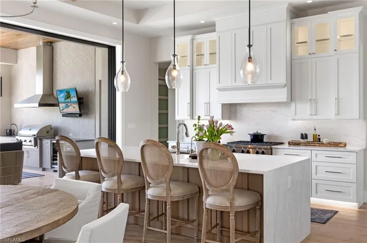 Kitchen featuring backsplash, light stone countertops, glass insert cabinets, hanging light fixtures, and a breakfast bar