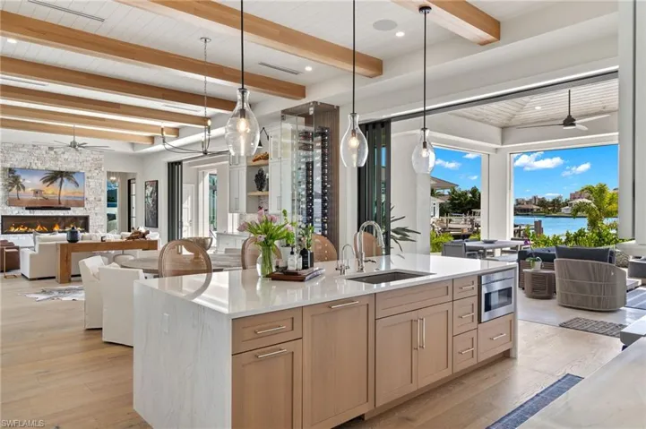 Kitchen featuring ceiling fan, open floor plan, light stone counters, and a wooden ceiling with exposed beams