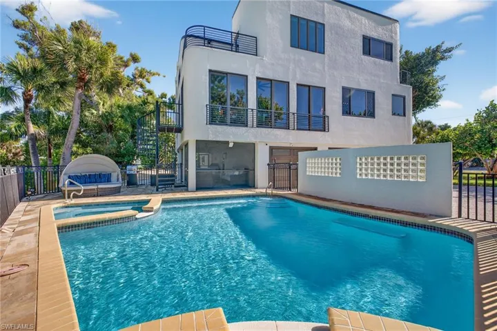 Back of property with a pool with connected hot tub, a balcony, stairs, stucco siding, and a patio