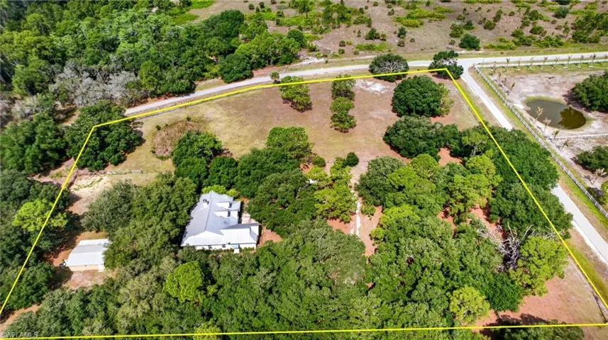 Expansive property featuring a single-story residence with a light-colored roof, surrounded by mature trees and natural landscaping
