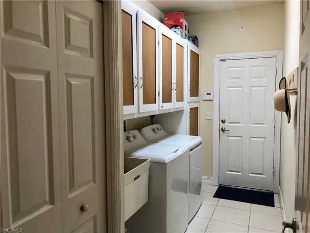 Laundry room featuring separate washer and dryer, light tile patterned floors, and cabinet space