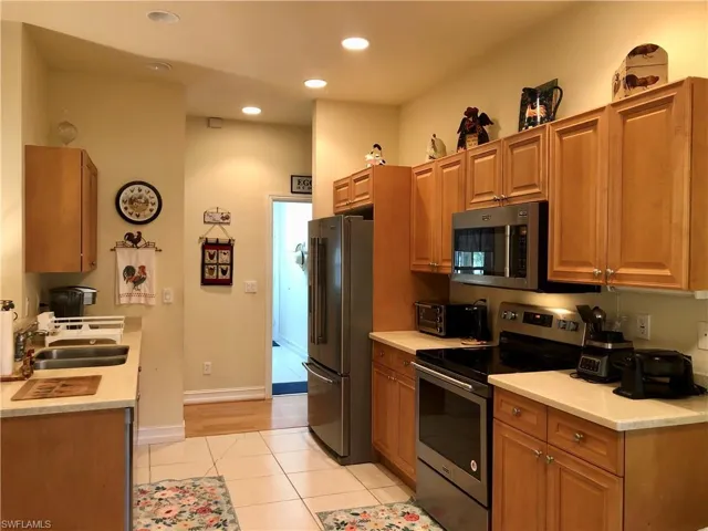 Kitchen with stainless steel appliances, wood finish cabinets, light tile patterned flooring, recessed lighting, and light stone counters