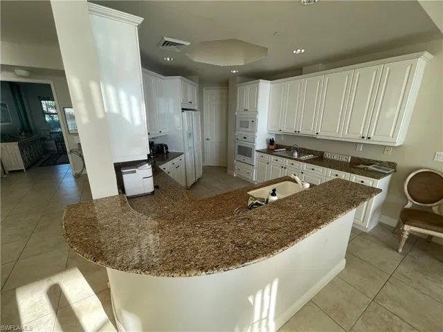 Kitchen featuring white appliances, a peninsula, visible vents, light tile patterned flooring, and a sink
