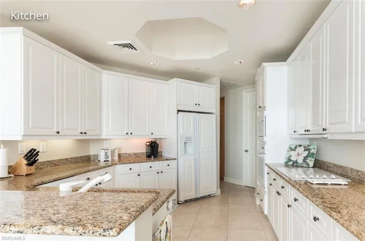 Kitchen with built in appliances, light tile patterned floors, light stone countertops, and white cabinets