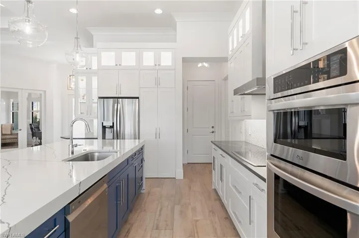 Kitchen with appliances with stainless steel finishes, ornamental molding, blue cabinetry, white cabinetry, and a sink